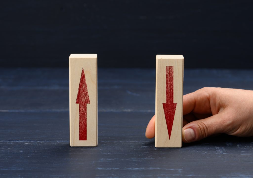 Female hand holds a wooden block with an upward arrow and down arrow, representing rise and fall.