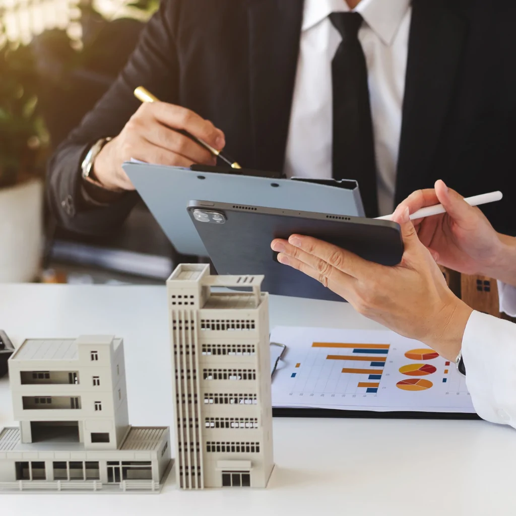 Two people reviewing property documents on tablet beside architectural building models