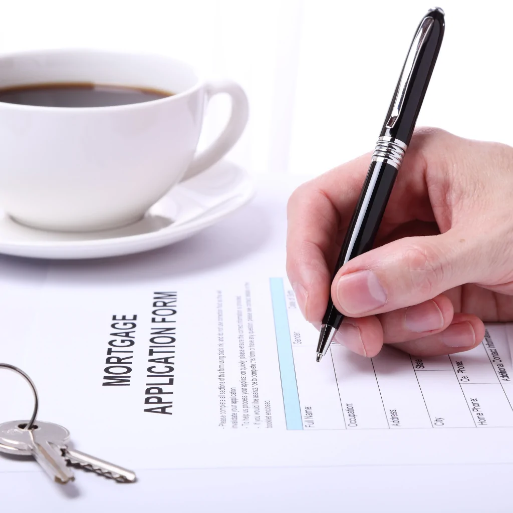 Person filling out a mortgage application form with pen, and house keys on desk