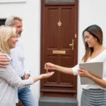 Couple handing house keys to new homeowner outside front door